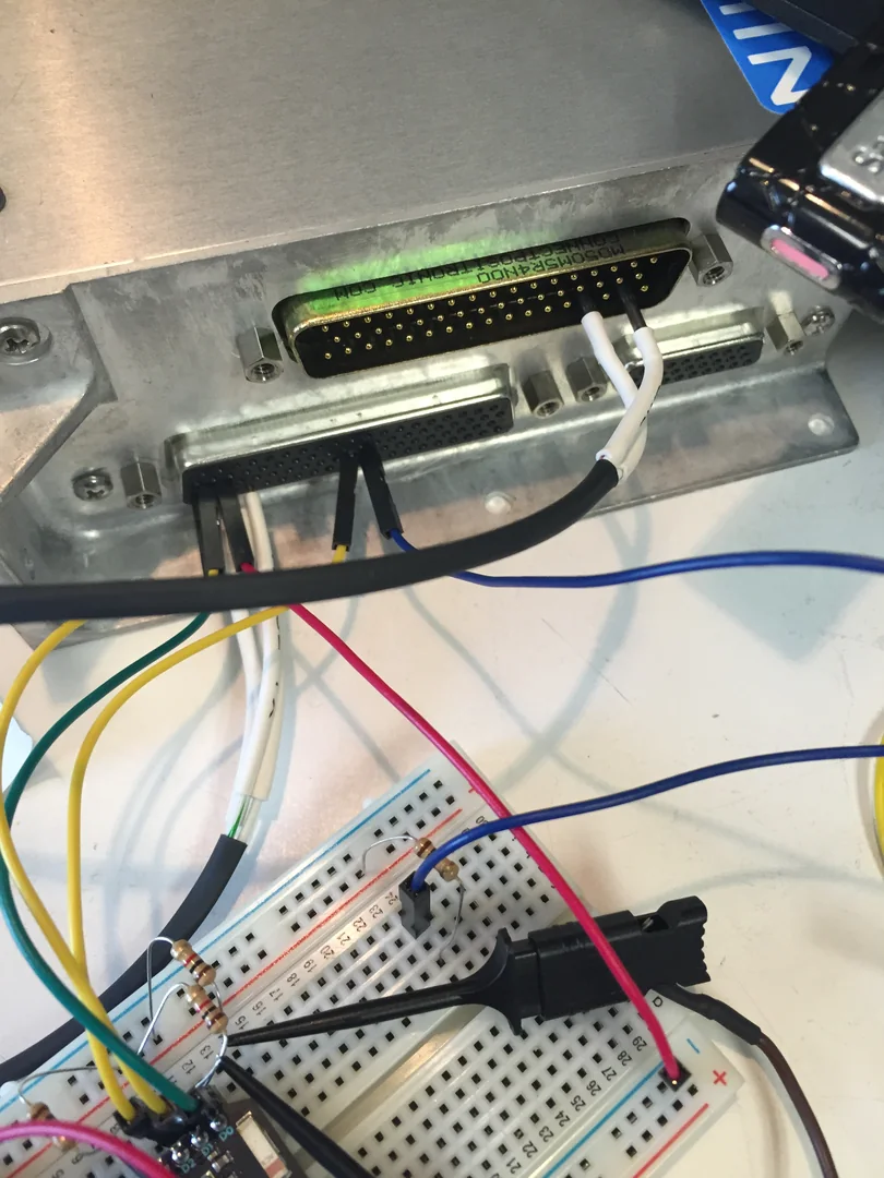 A microcontroller and breadboard connected to avionics hardware on a test bench